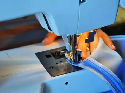 Close-up of a sewing-machine needle stitching a blue hem