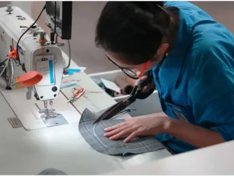 A worker trimming a fabric panel with shears at a sewing machine