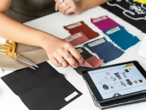 Hands comparing fabric swatches beside a tablet showing a design board