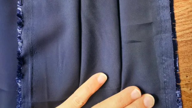 A hand checking the edge of a navy sweatshirt fabric panel