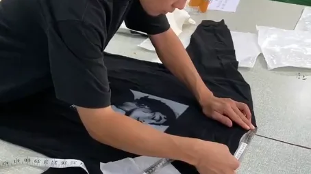A worker measuring a black garment with a tape measure at an inspection table