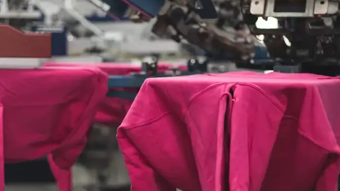 Pink sweatshirts on the bed of a heat press on the production floor