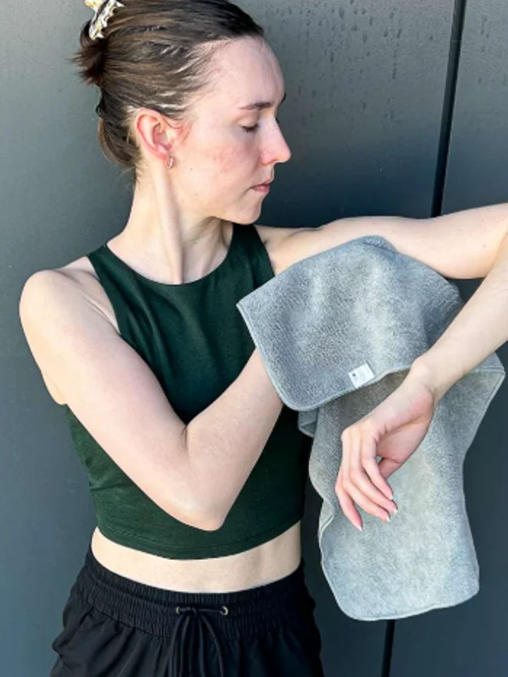 Dabbing a grey towel against a raised arm, in front of a dark grey wall