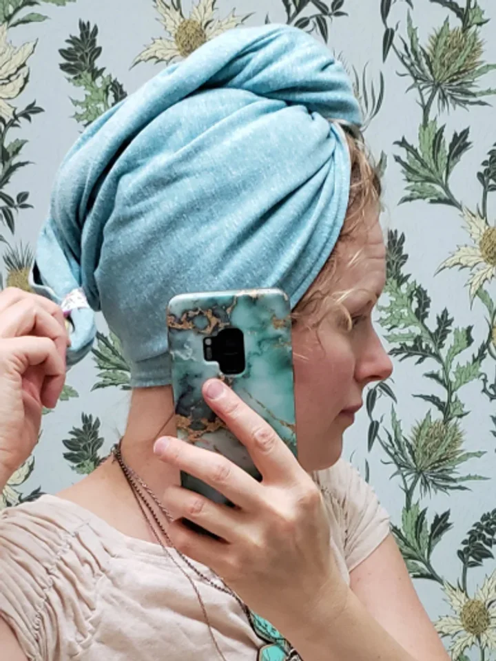Light blue hair turban wrapped over wet hair, a phone held up in one hand