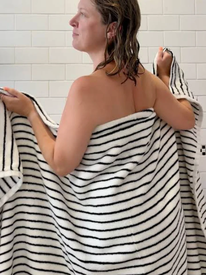Wrapped in a striped bath sheet, a woman stands with her back to a tiled wall