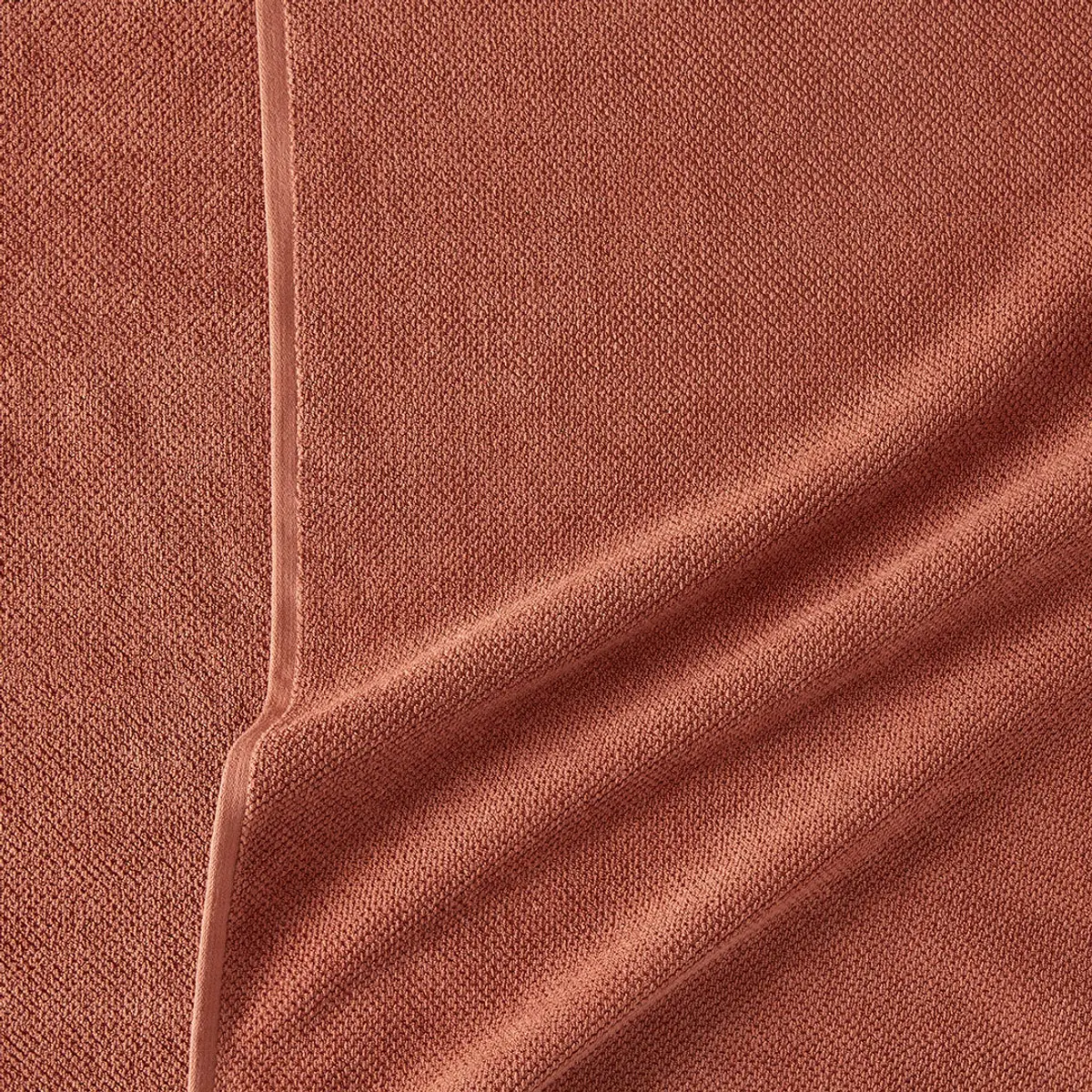 The fine weave of a rust-coloured cotton cloth, a narrow seam running through it