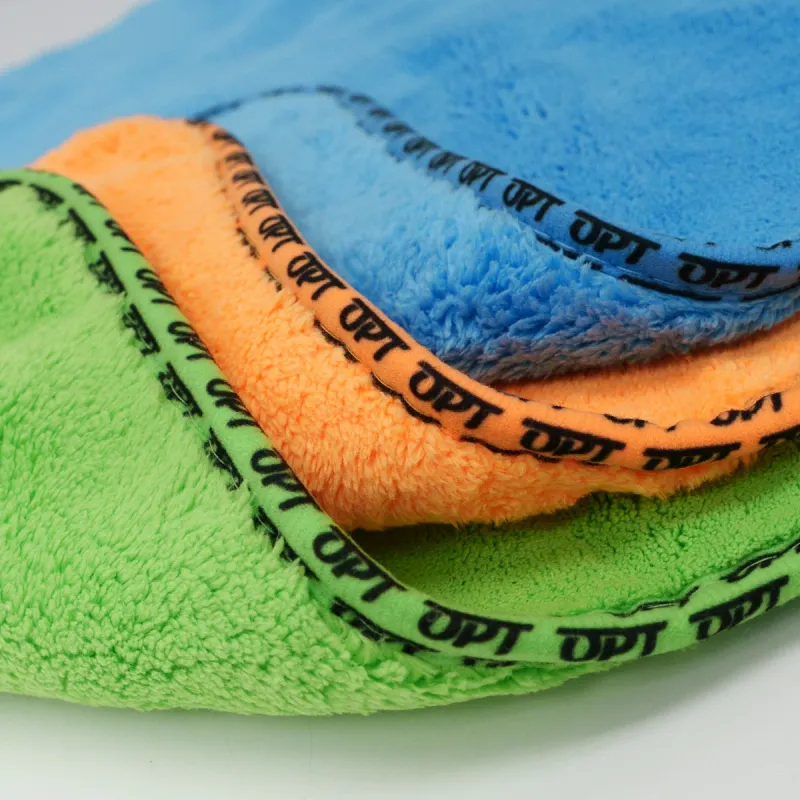 Microfibre cloths in green, orange and blue, their edges bound in a printed tape