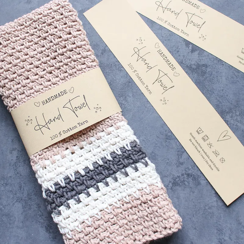 Crocheted hand towel wrapped in a kraft band reading Hand Towel, beside two matching kraft tags