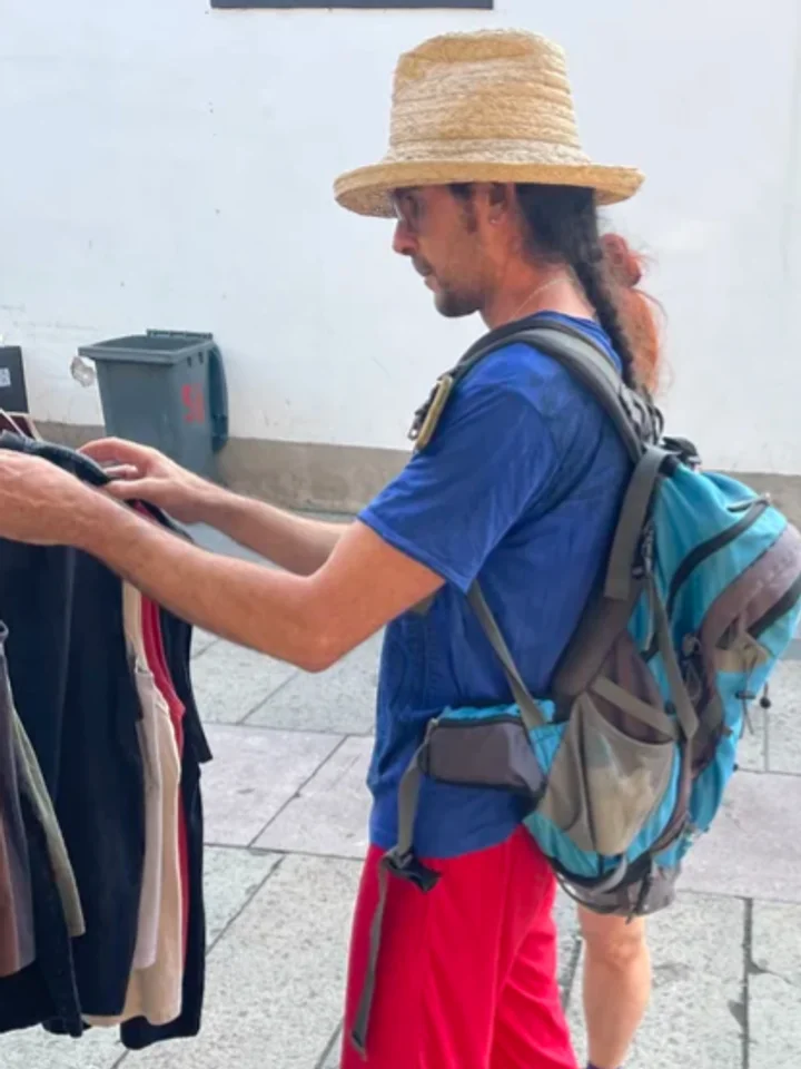 A customer in a bright blue t-shirt and shorts on the street, backpack on
