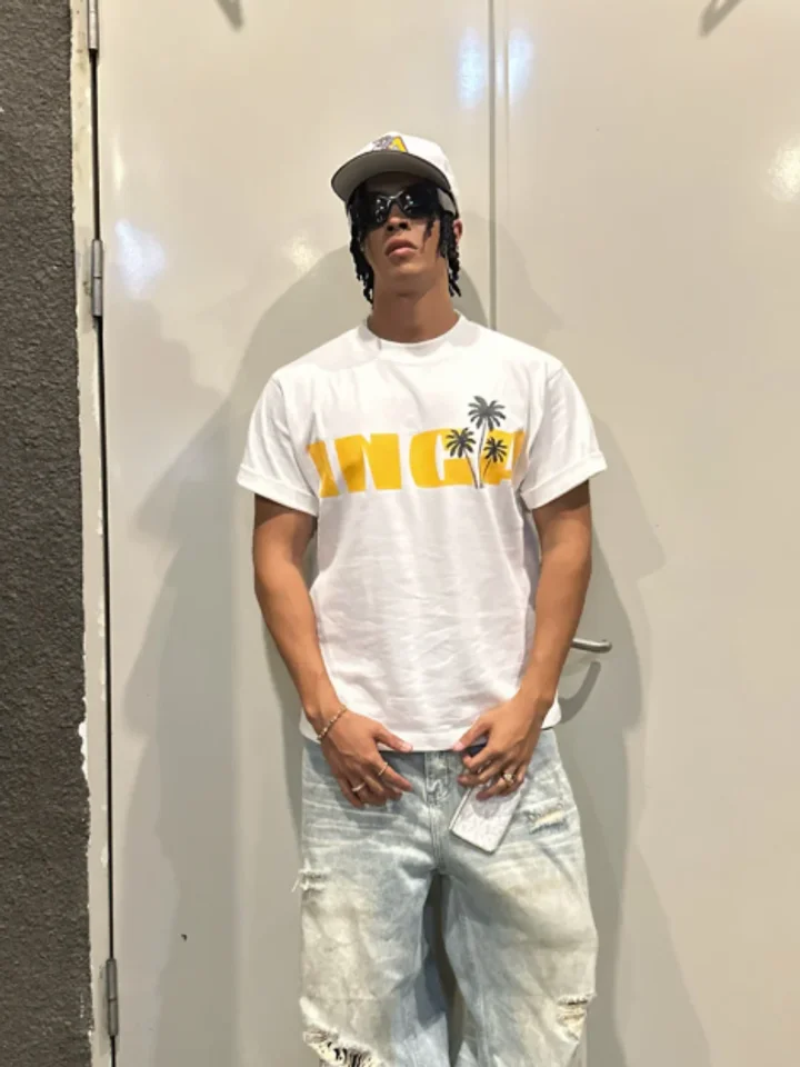 A customer in a white graphic t-shirt with a yellow palm print, cap and sunglasses